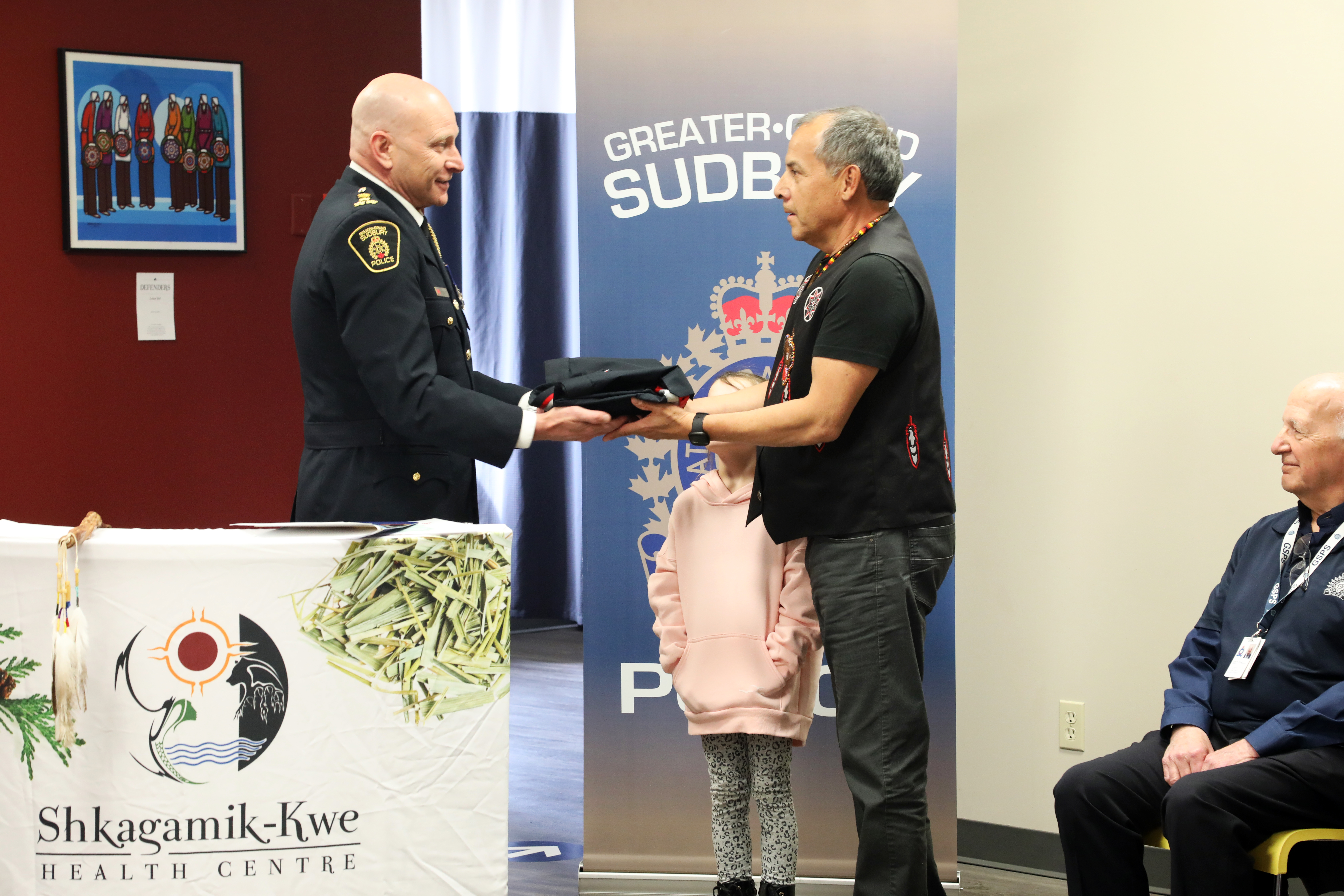 Chief Pedersen gifts a ribbon shirt to George Couchie chief of police handing ribbon shirt to man