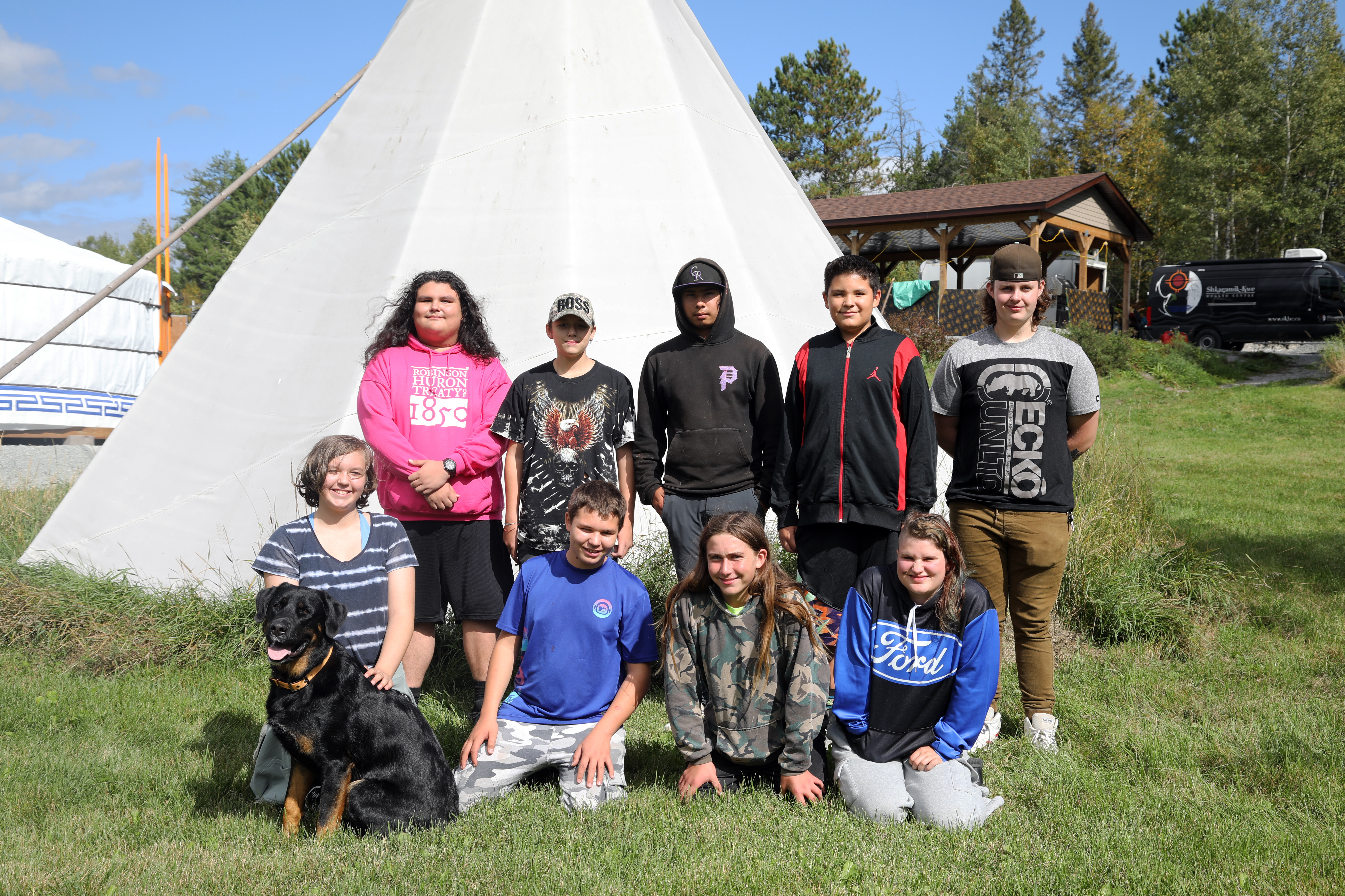 Moose Hunt youth participants youth smiling outside with dog in front of tipi