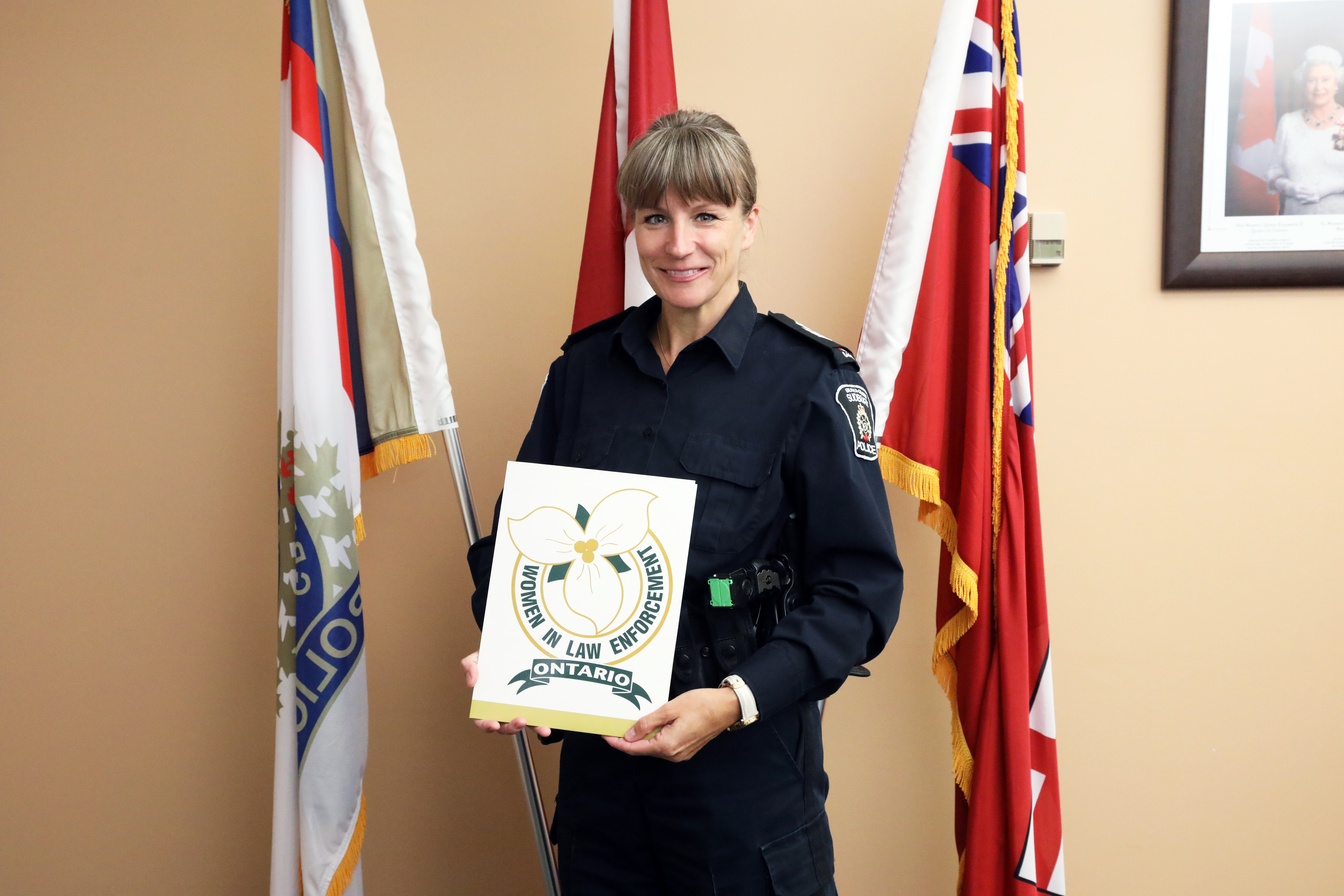 Staff Sergeant Laura Wawryszyn with her OWLE nomination police officer standing in front of flags holding nomination certificate